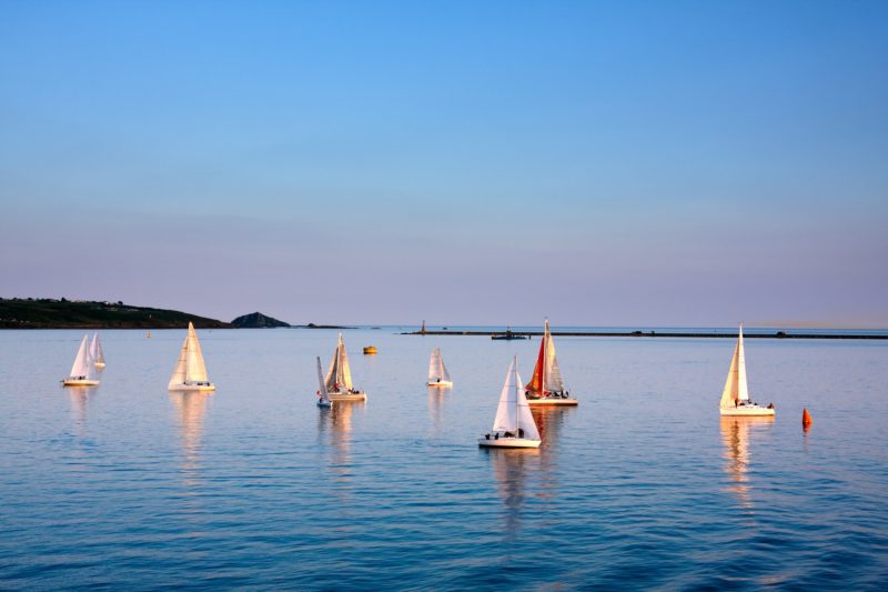 several white and red sailing boats on the calm blue sea in Plymouth Sound just before sunset with a the sky starting to turn pink