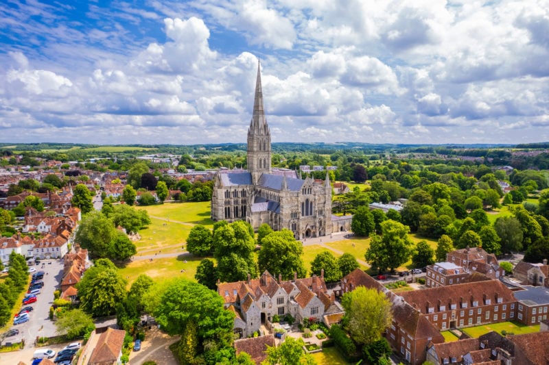 Aerial view of Salisbury Cathedral and the surrounding town centre on summer day. the cathedral is stood on a grassy lawn surrounded by small leafy trees. Most beautiful cities in England.