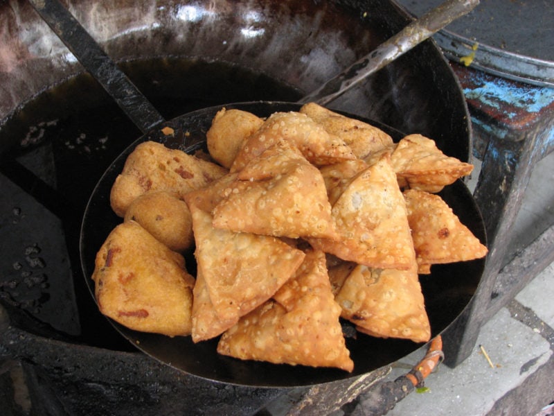 close up of a large black frying pan filled with traingle pastry samosas frying 