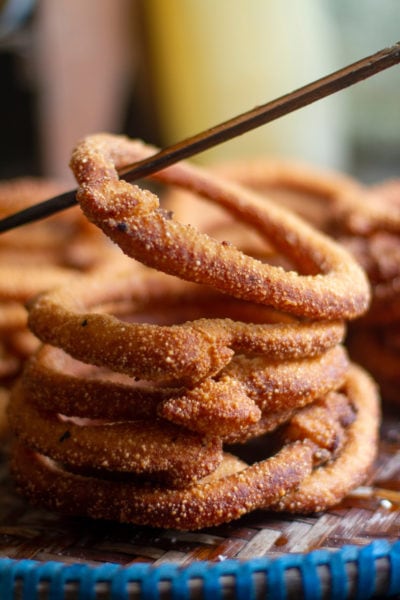 stack of sel roti, thin circles of doughy bread, the top one is being picked up by a chopstick