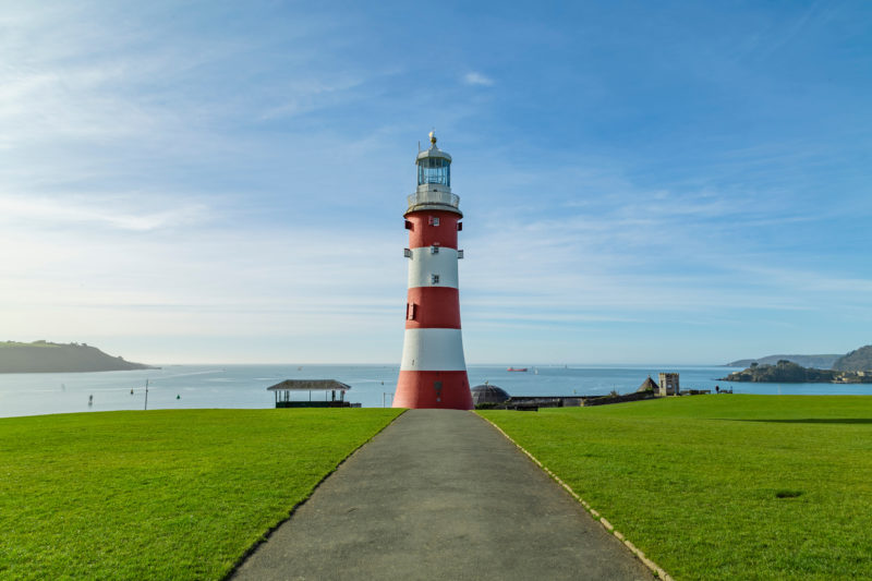 path leading through a grassy lawn towards a red and white lighthouse tower on a cliff overlooking the sea