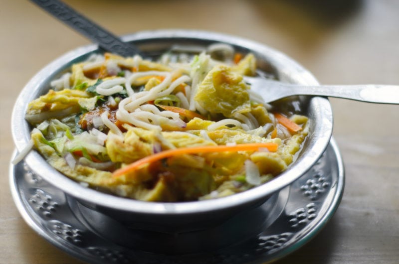 close up of a small metal bowl on an engraved metal plate filled with noodles and soup with shredded carrot and other vegetables. What to eat in Nepal. 