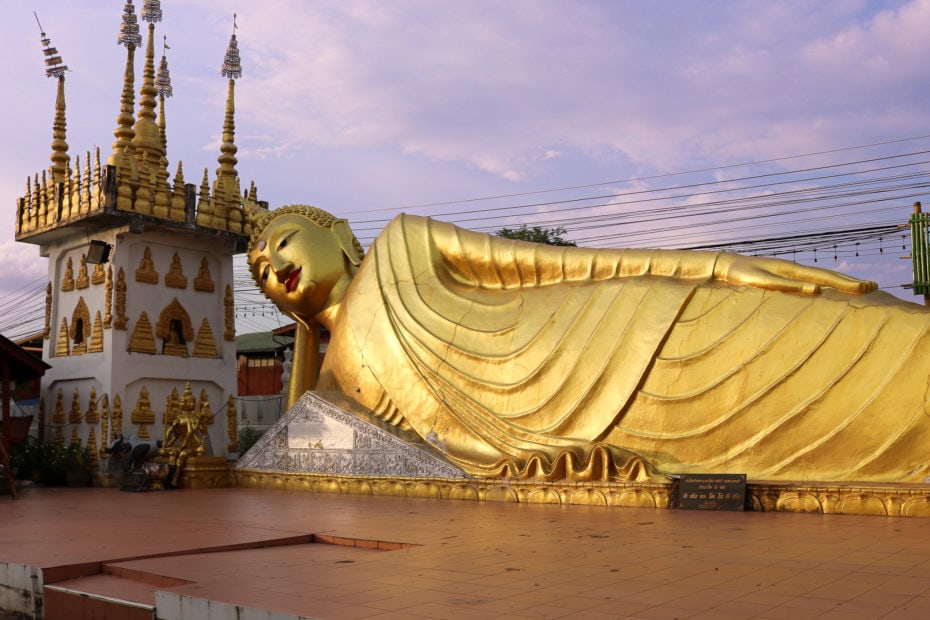 large golden statue of a buddha lying on its side wiht its head on one hand and the other arm lying on its side at a temple in phrae thailand