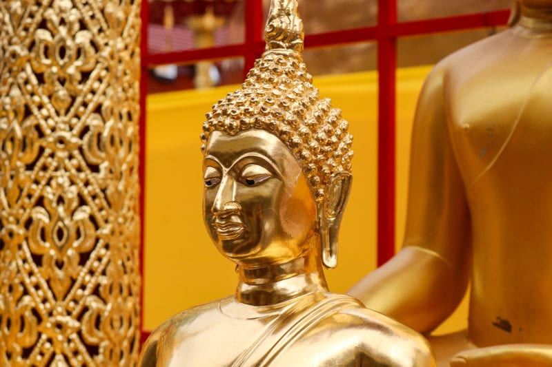 close up of a golden buddha statue's head and shoulders with gold temple wall behind