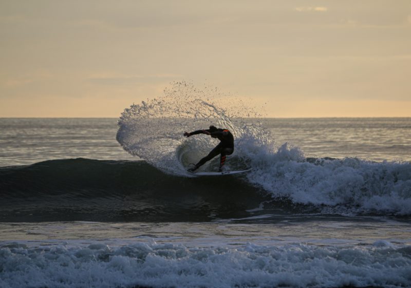 man surfing on sea waves in croyde north devon just after sunset with the surfer silhouetted against a yellow-gold sky 