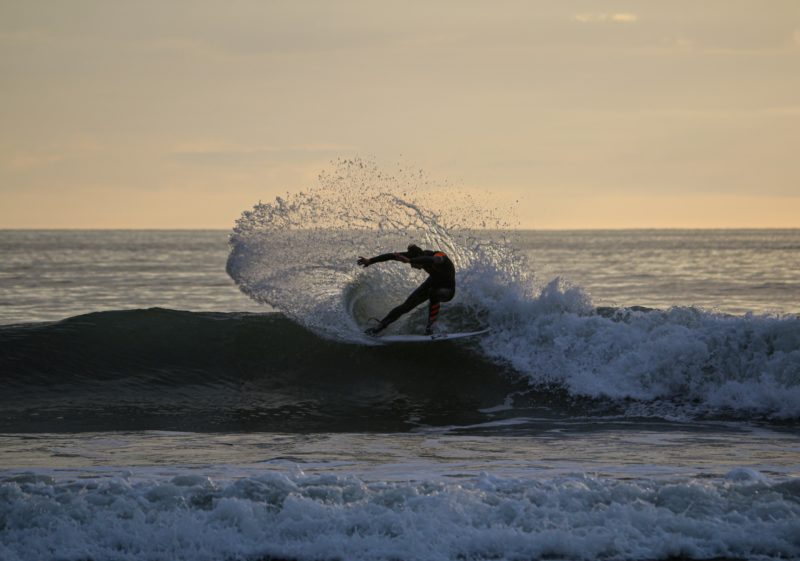 man surfing on sea waves in croyde north devon just after sunset with the surfer silhouetted against a yellow-gold sky