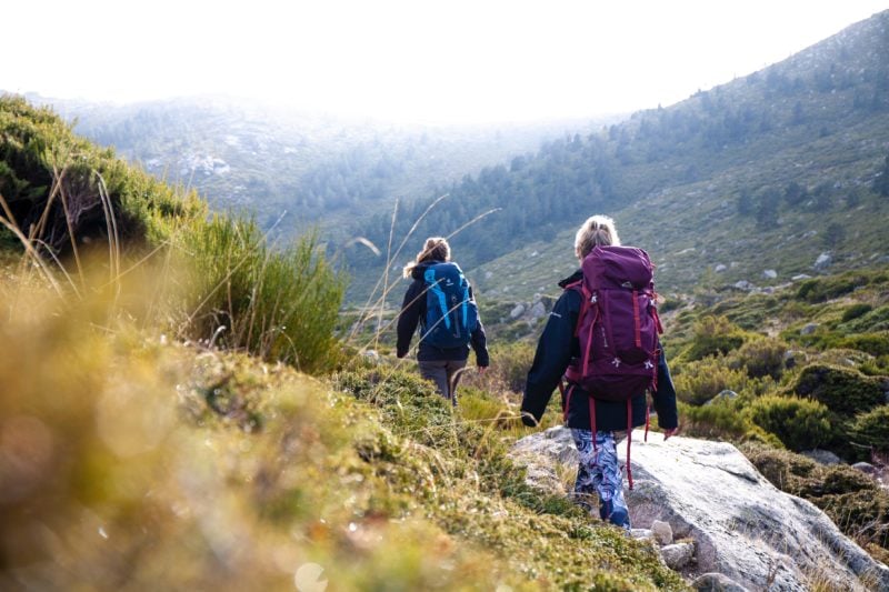 2 women carrying large backpacks hiking on a rocky mountain path in Guadarrama National Park near Madrid Spain