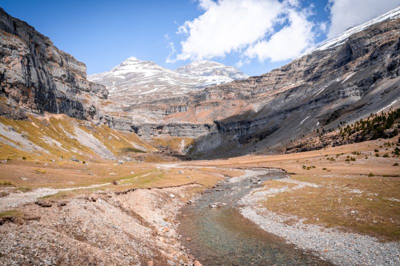 shallow winding river in a valley surrounded by rocky snowcapped mountains