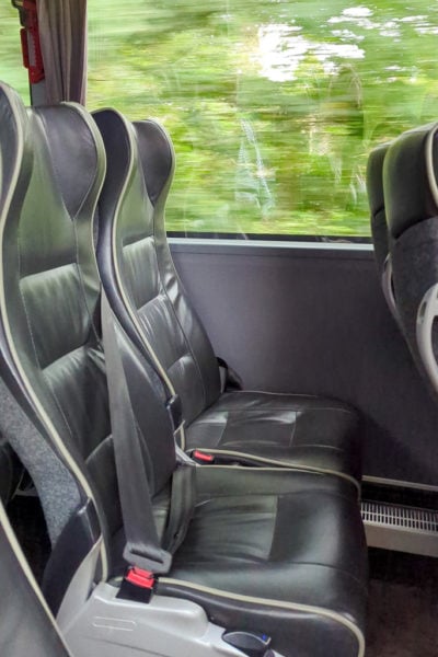 two black leather seats on a moving bus with a blurred view of green trees out the window