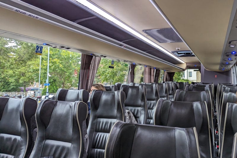 interior of a coach with black leather seats and large windows with a view of green trees
