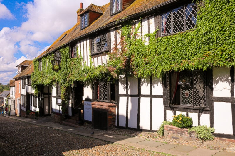 cobbled street with a large medieval half timbered inn painted white with dark wood timbers and lots of ivy growing on the facade