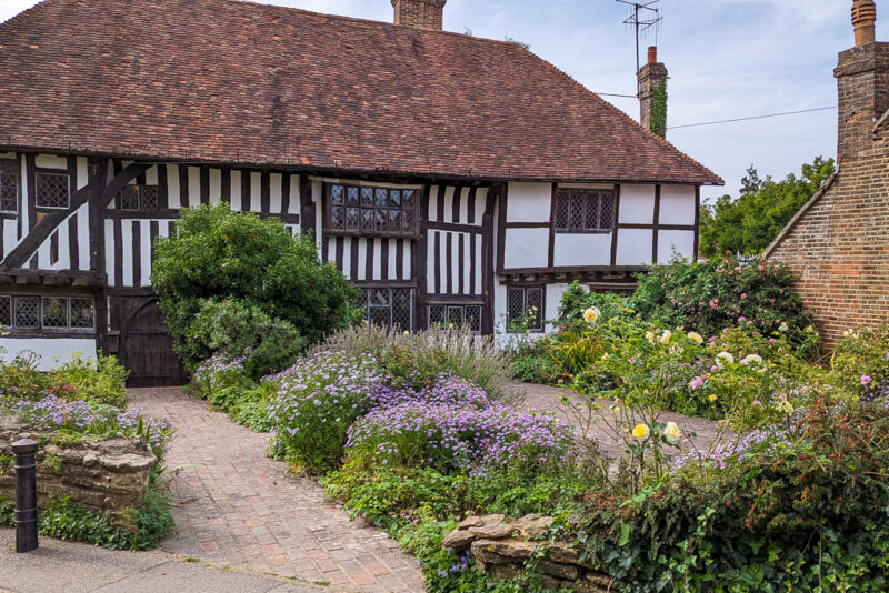 timber frame house with red tiled roof and white walls with a garden filled with many colourful flowers