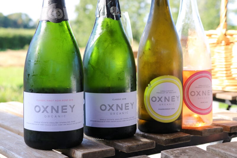 close up of four Oxney Organic Estate wine bottles on a wooden table outside on a sunny day. Things to do in 1066 Country East Sussex England. 