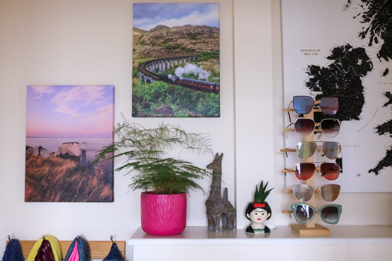 two canvas prints on a white wall above a shelf with a plant pot and some ornaments, one print has a steam train in a green valley and the other has some chalk rock stacks at sunset with a pink sky. MYPICTURE canvas prints review. 