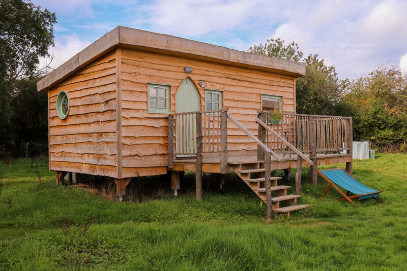 wooden cabin with a terrace and a light green front door in a grassy field at Starcroft Farm Cabins - glamping near Battle, East Sussex England