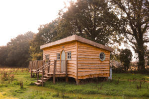 wooden cabin with a terrace in a grassy field with the sun setting through the trees behind. Starcroft Farm Cabins review, glamping in East Sussex England