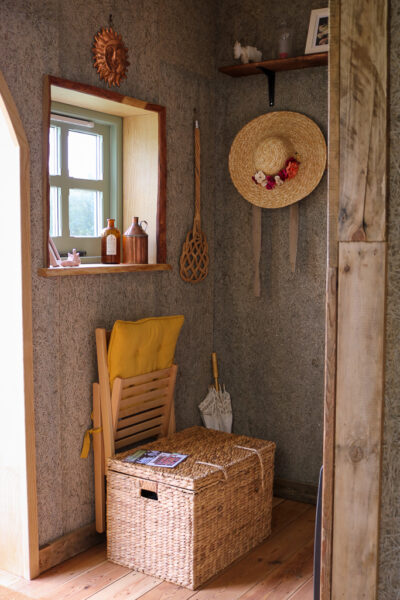 interior of a wooden cabin with grey walls and a small window. there is a wicker hamper and a straw hat hanging from a peg on the wall. Starcroft Farm Cabins review, glamping in East Sussex England