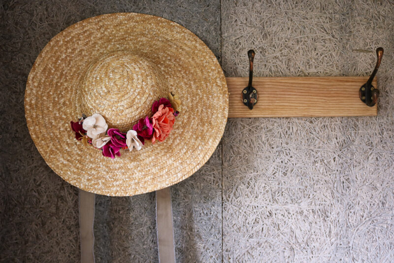 close up of a coat rack with a straw bonnet hanging from one of the pegs