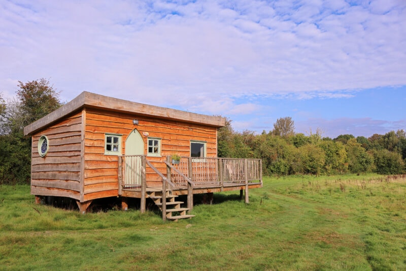 wooden cabin with a terrace and a light green front door in a grassy field. Starcroft Farm Cabins review - glamping battle east sussex england