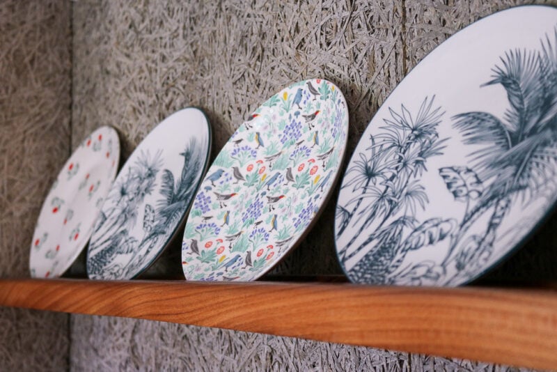 close up of some patterned china plates on a wooden shelf on a grey wall