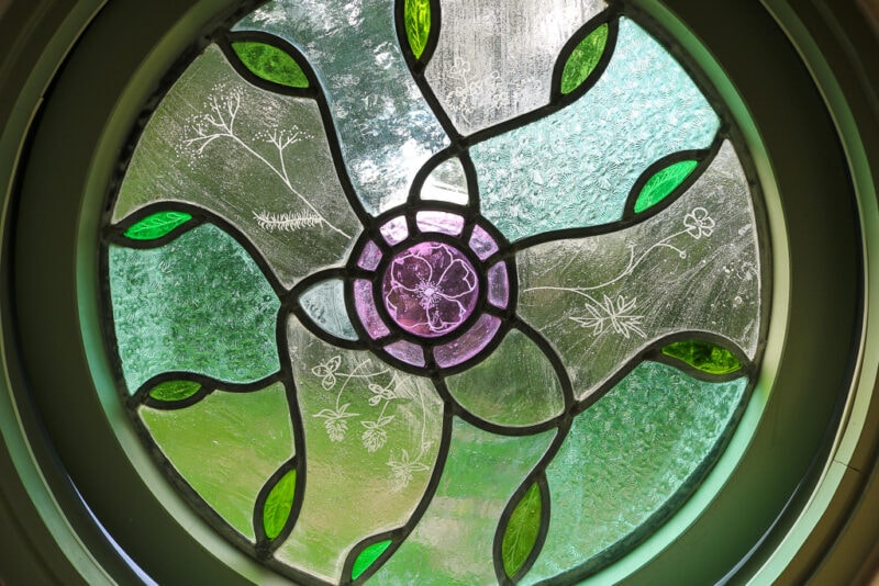 close up of a circular stained glass window with green leaves around a pink flower