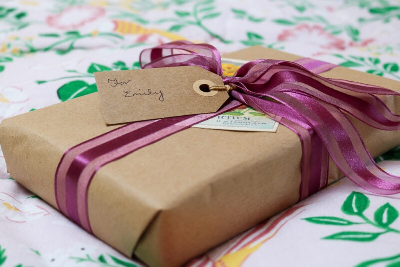 close up of a gift wrapped in brown paper with a pink ribbon - gift ideas for travel lovers