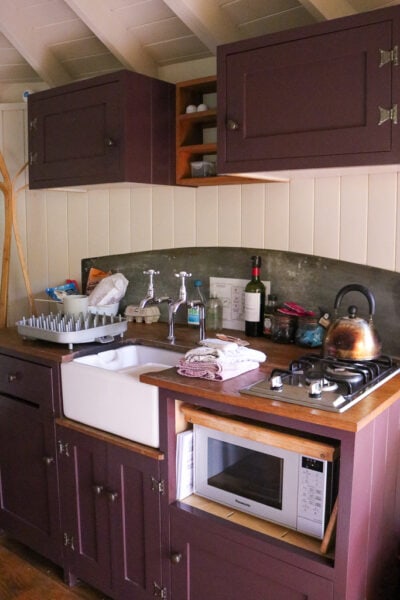 interior of a wooden cabin with cream coloured panels with a small kitchenette with purple cupboards and a large white sink