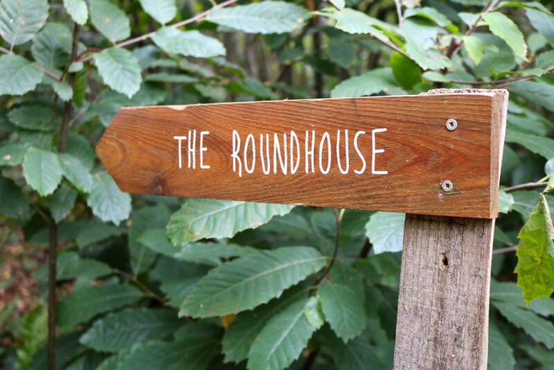 close up of a wooden arrow shaped signpost with white writing that says "the Roundhouse"