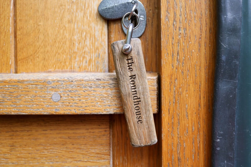 close up of a key in the lock of a wooden door with a large wooden keyring that says "the roundhouse"