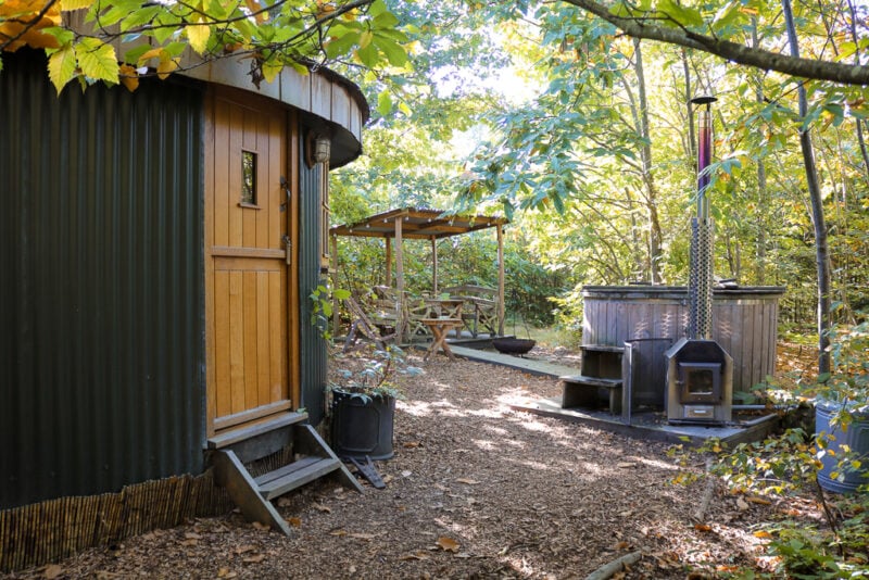 circular wooden cabin with green pannelled exterior and a light brown wooden door in a woodland with a large oak tree behind. Swallowtail Hill glamping review Rye, East Sussex