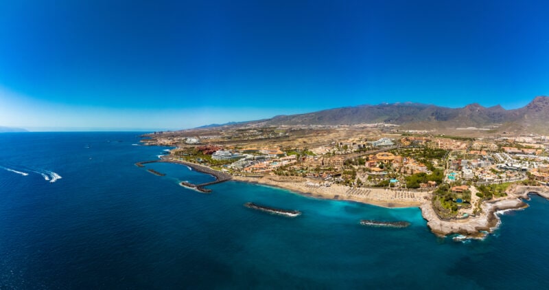 aerial view of White sandy El Duque beach and coastline in Tenerife with brown mountains in the background