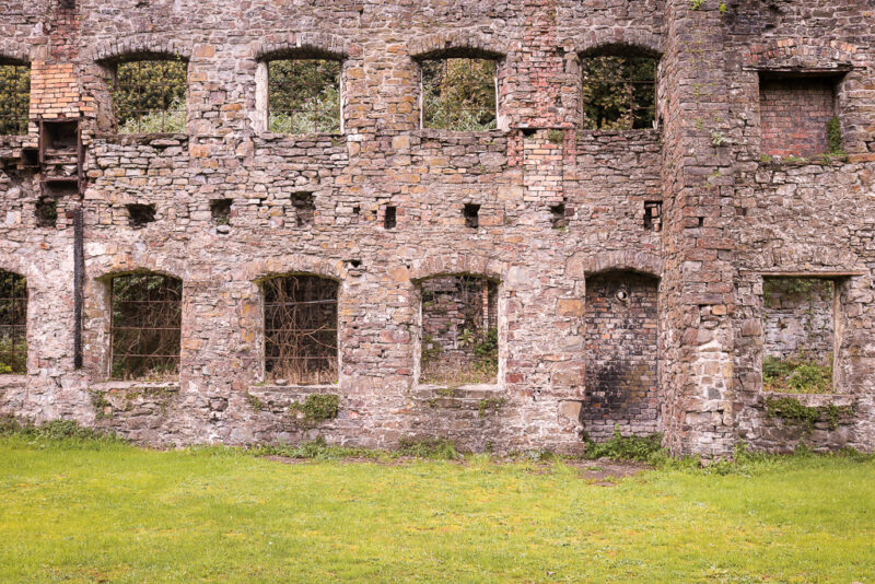 ruined stone wall of an old ironworks building in Neath with many empty windows looking out at trees behind