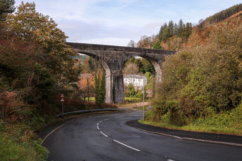 stone arches of an aqueduct above a tarmac road with autumnal trees on either side