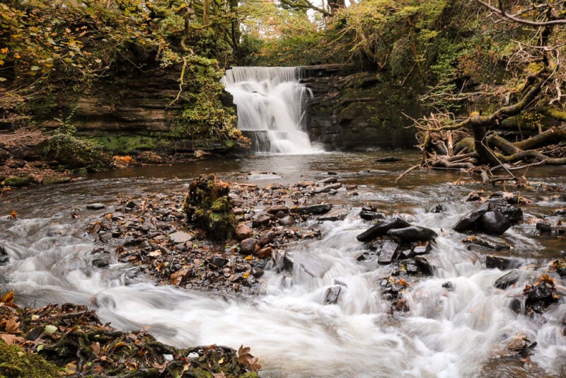 small waterfall above a river with blurred white water motion in a small woodland. Neath Abbey Waterfall. 