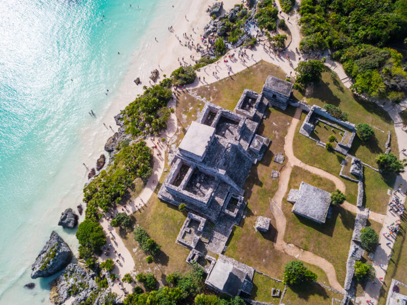 aerial view of some grey stone mayan ruins on a clifftop overlooking turquoise sea