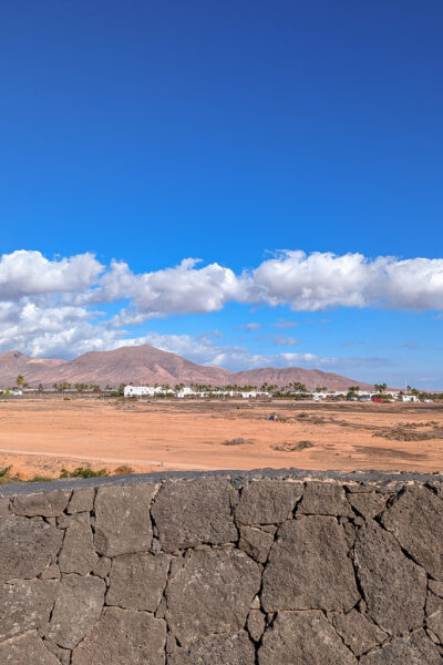 stone wall with a view of distant orange coloured volcanic hills on a sunny day with blue sky above