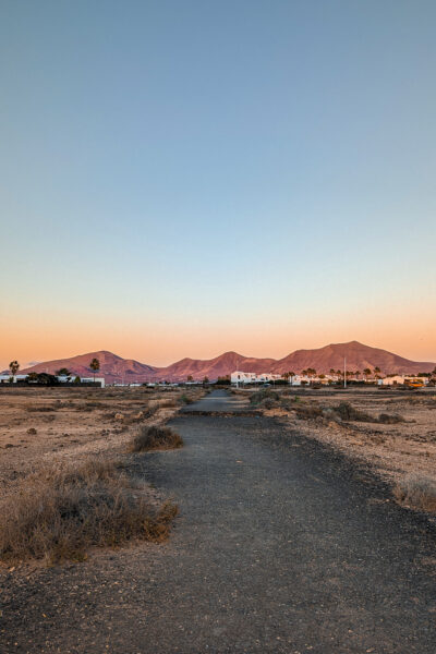 looking down a road towards red-brown volcanic hills just before sunset with the horizon glowing orange behind the hills. Lanzarote in winter. 