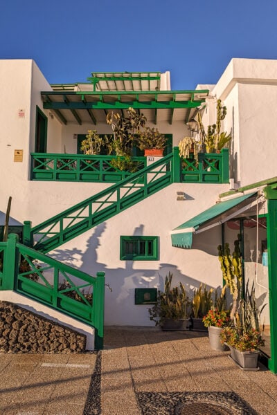 white two storey villa with bright green wooden trim around the outside staircase and second floor terrace