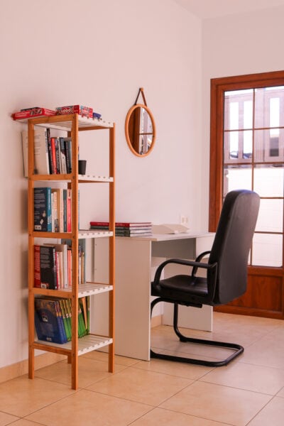 white wooden desk with a black office chair next to a small wooden bookshelf with patio doors behind