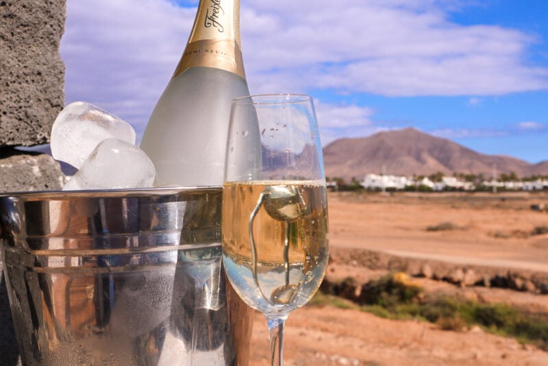 glass of cava next to a silver bucket filled with ice and a bottle of cava, with a view of a brown volcanic mountain behind. Review of Playa Blanca Holiday Villas in Lanzarote. 