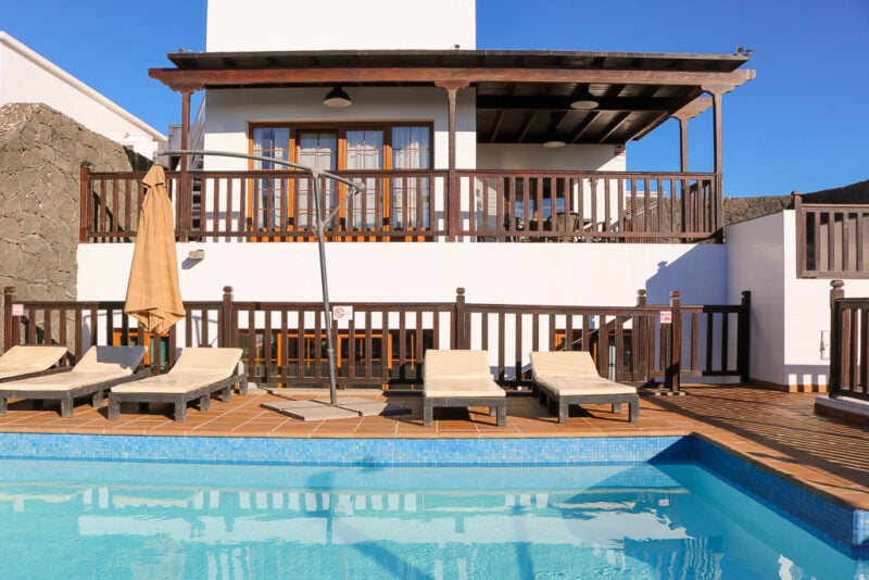 small outdoor swimming pool in front of a white painted two storey villa with wooden trim on a sunny day with blue sky. Playa Blanca Holiday Villas in Lanzarote. 