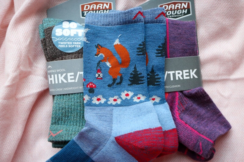 three pairs of Darn Tough wool hiking socks in teal, blue and purple (from left to right) on a pink blanket