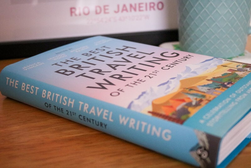 blue hardback book on a table next to a green coffee mug with the title The Best British Travel Writing of the 21st Century on the cover 