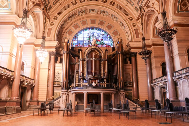 interior of the concert hall in St George's Hall Liverpool with an arched carved cieling and many pillars along the side around a wooden floor. There is a huge organ on the far wall above the dance floor.