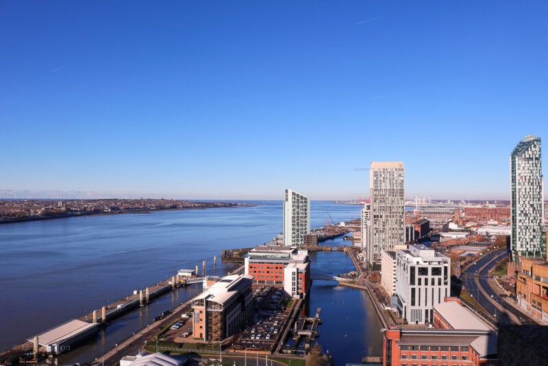 looking down at a wide blue river next to part of a city with several tall tower buildings on a sunny winter day with clear blue sky above. Liverpool city break travel guide 