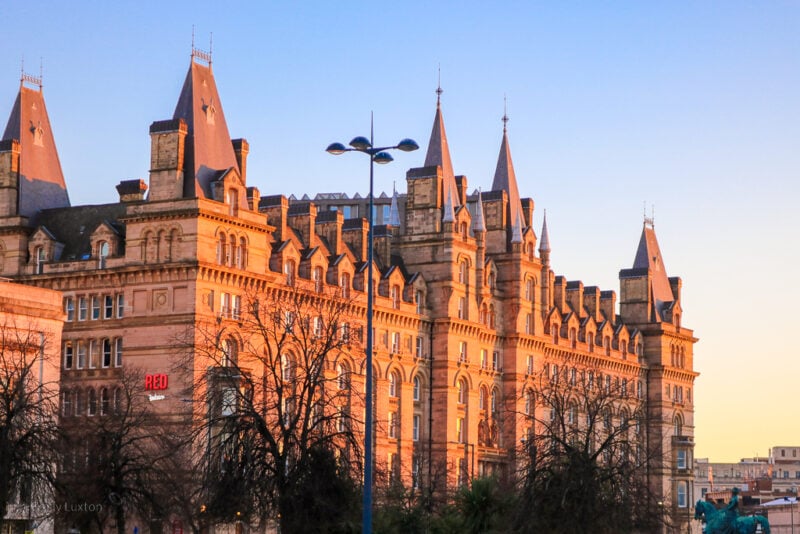 Exterior of the Radisson RED hotel in Liverpool, a very grand building in reddish beige stone taken during golden hour before sunset with a strong orange glow reflecting off the building.