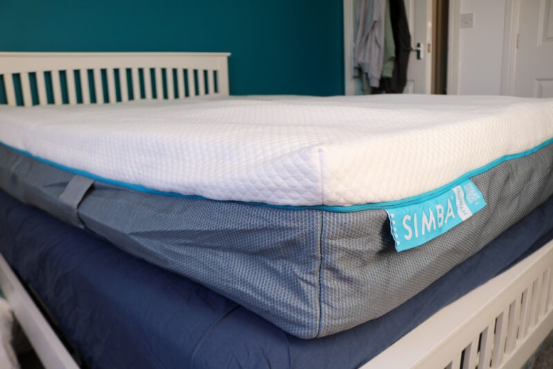 Partially inflated matress with a grey base and white top on top of a white wooden bedframe with a navy blue sheet underneath