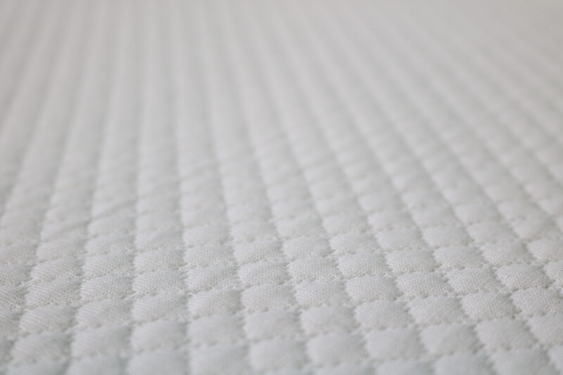 Close up of a section of a white mattress with a soft patterned top on