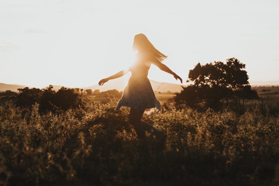 silhouette of a girl spinning in a field of long grass with the sunset behind