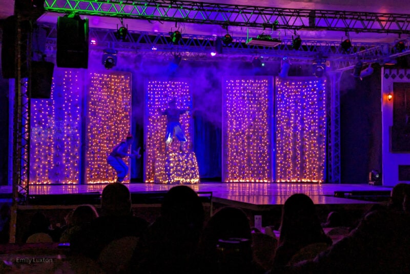 dark stage with curtains of fairy lights and the figures of aladdin and the genie silhouetted against them